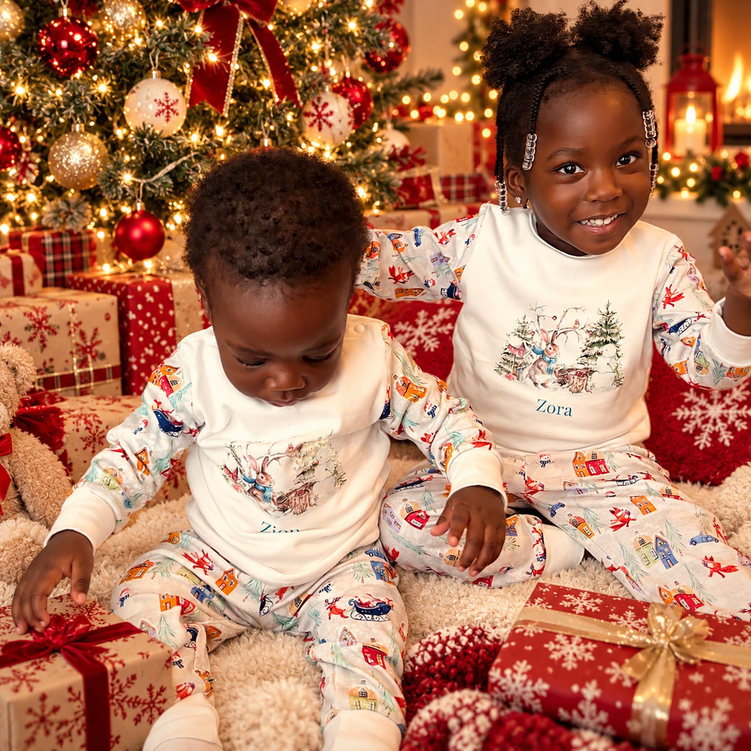 Two children wearing matching personalised Christmas pyjamas by a decorated Christmas tree with red and gold presents